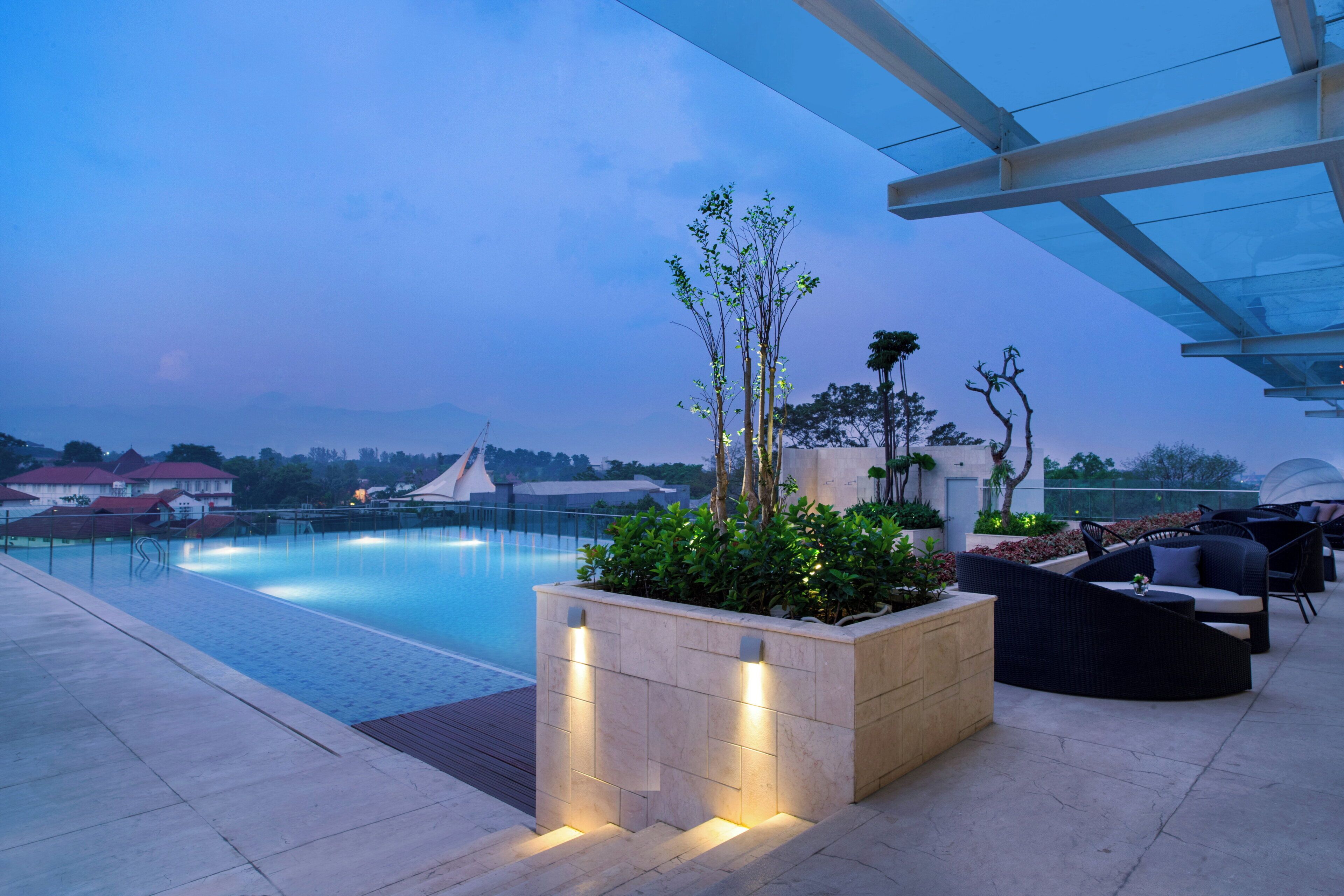 Área de piscina en la azotea con una cubierta de vidrio, asientos y vistas de los edificios circundantes.