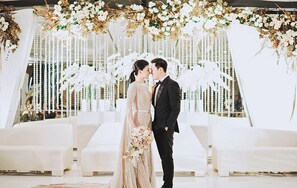 Une cérémonie de mariage avec un décor floral blanc en arrière-plan et une disposition des sièges.