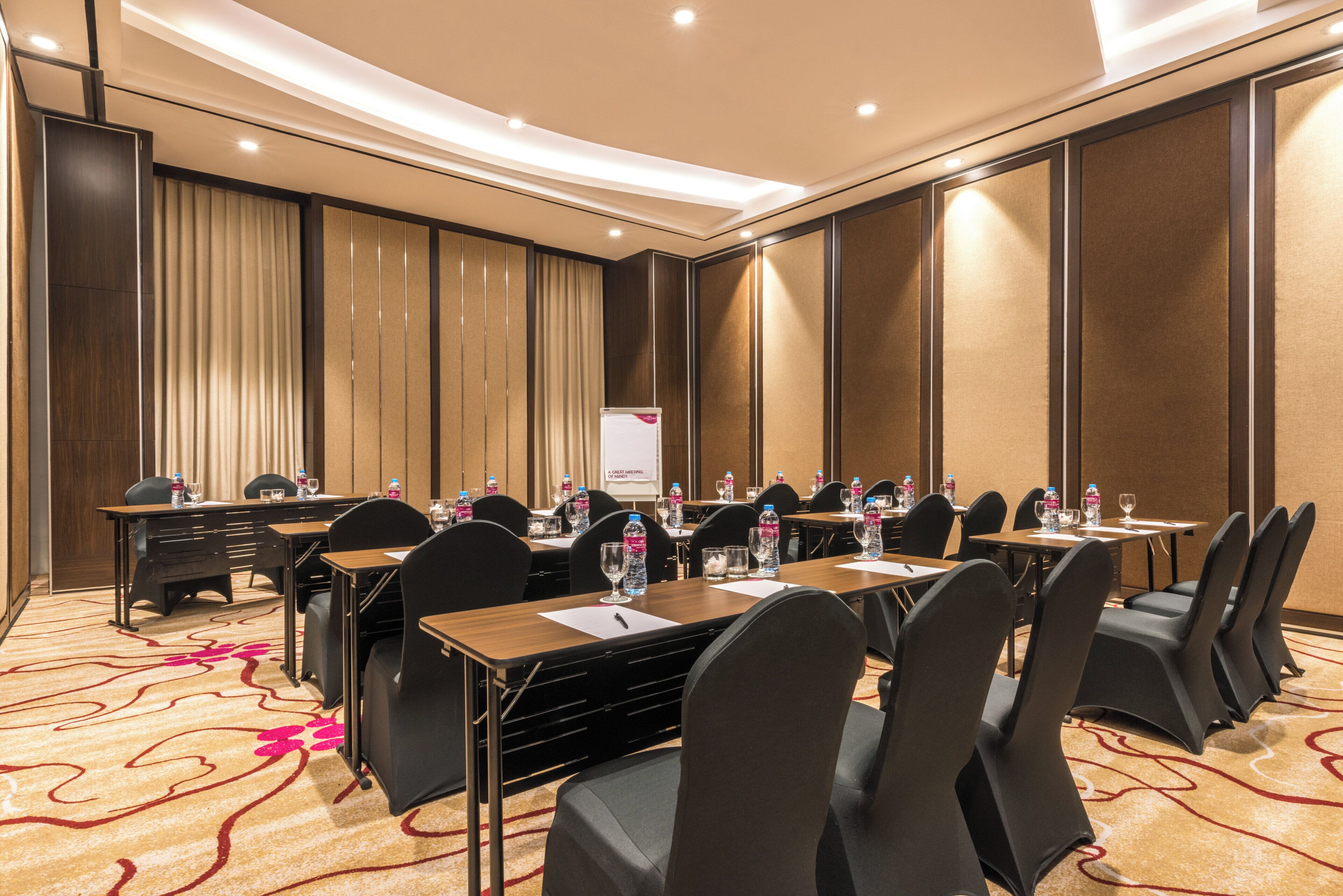 A conference room with multiple tables and chairs, equipped with water bottles and glasses, and a banner on the wall.