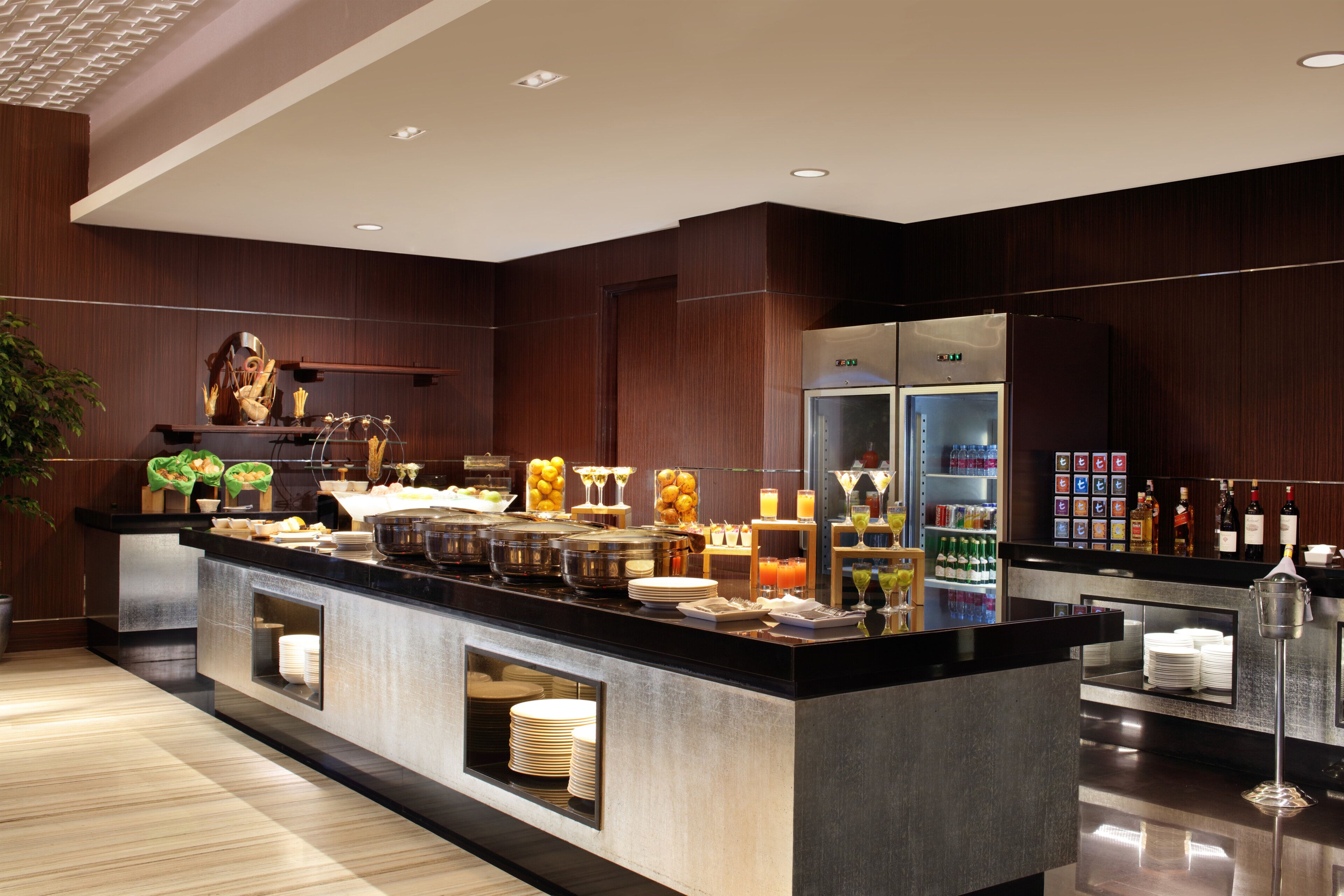 A modern hotel breakfast bar with a variety of food and drink options, a refrigerator, and a buffet area.
