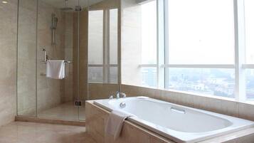 Un baño moderno con ducha envuelta en cristal, una bañera grande y vistas a la ciudad a través de amplios ventanales.