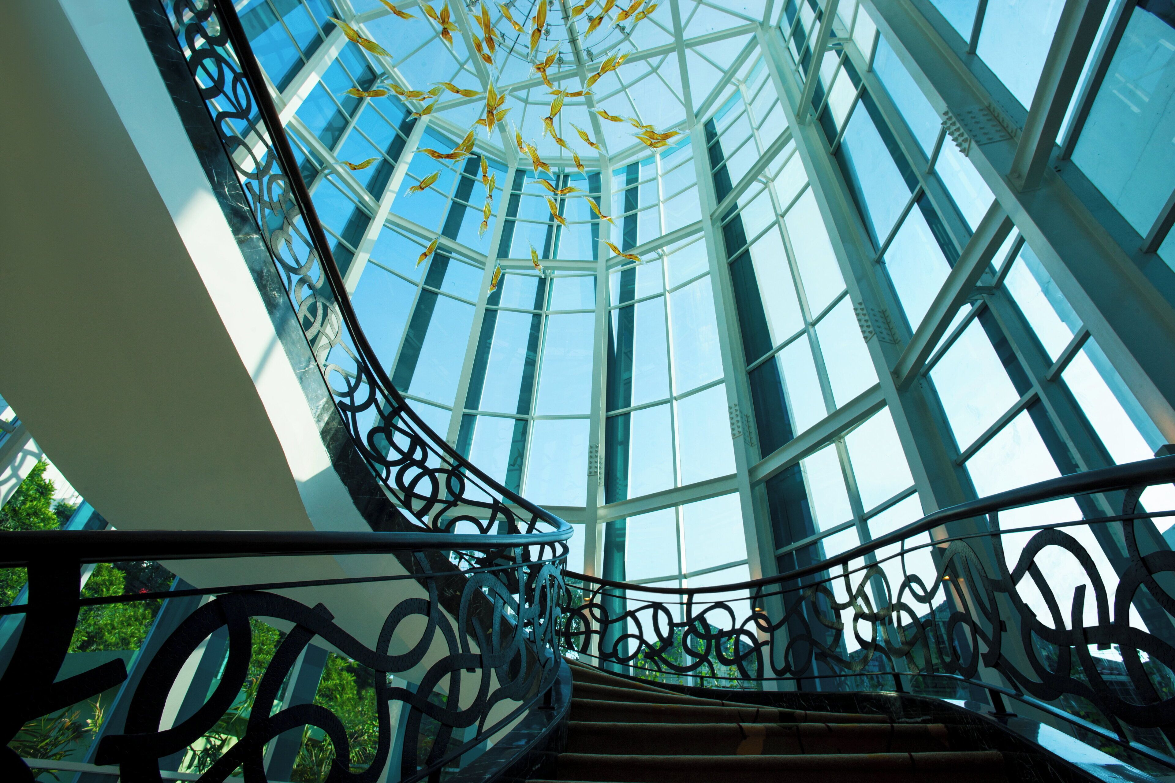 A spiral staircase with glass railings leading to a high ceiling with a skylight.