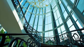 A spiral staircase with glass railings leading to a high ceiling with a skylight.