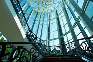 A spiral staircase with glass railings leading to a high ceiling with a skylight. - Crowne Plaza Bandung by IHG (Bandung)