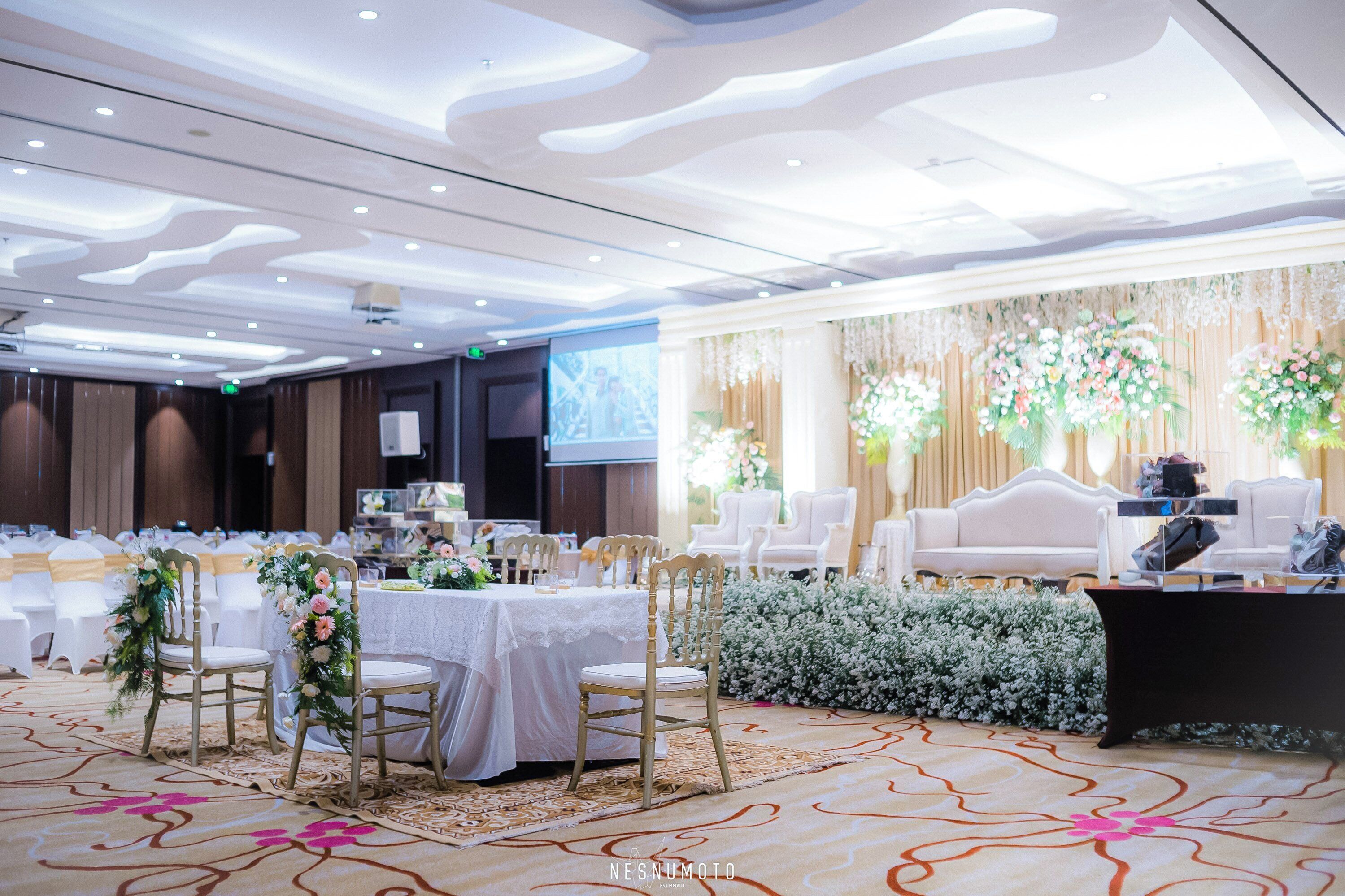 Een balzaal met ronde tafels, witte stoelen en bloemendecoraties.