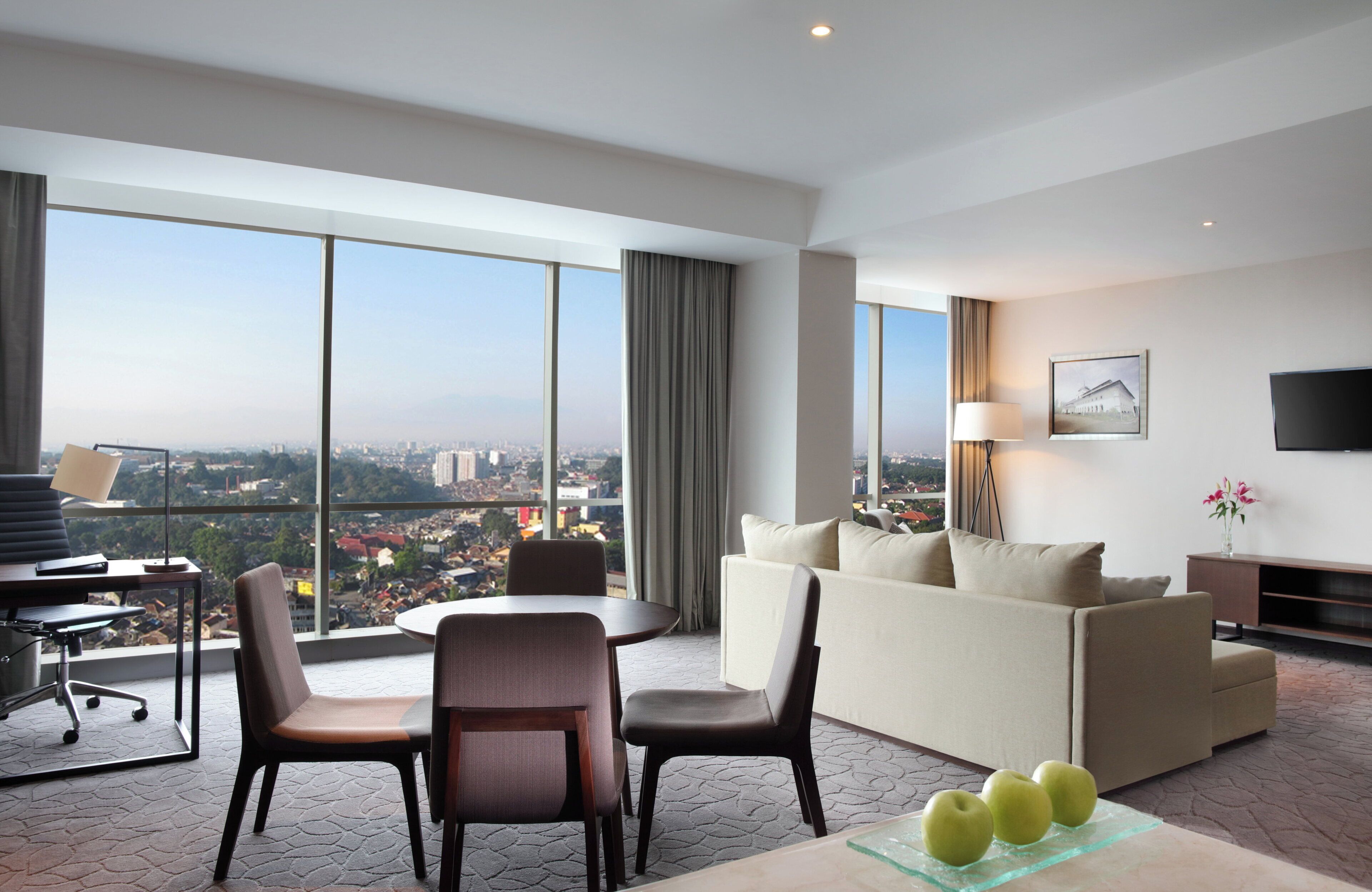 A modern hotel room with a city view, a dining area, and a living space with a sofa and a TV.