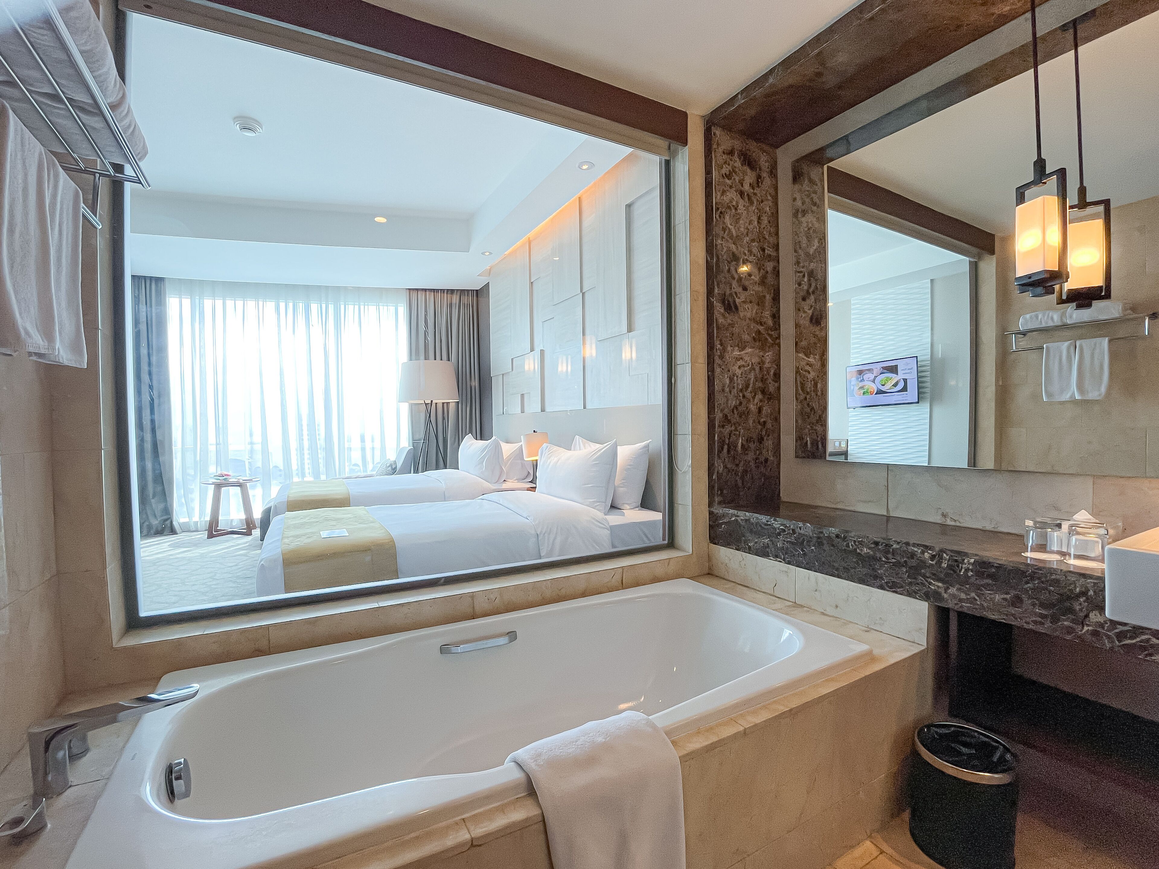 Une salle de bain d’hôtel moderne, dotée d’une grande baignoire, d’un meuble-lavabo avec miroir et offrant une vue sur la chambre.