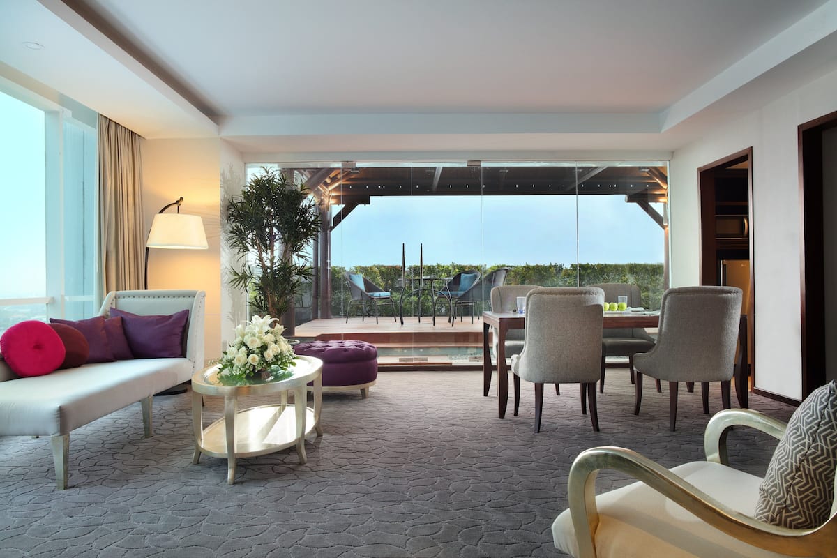 A modern hotel room with a balcony, furnished with a sofa, chairs, and a dining table.