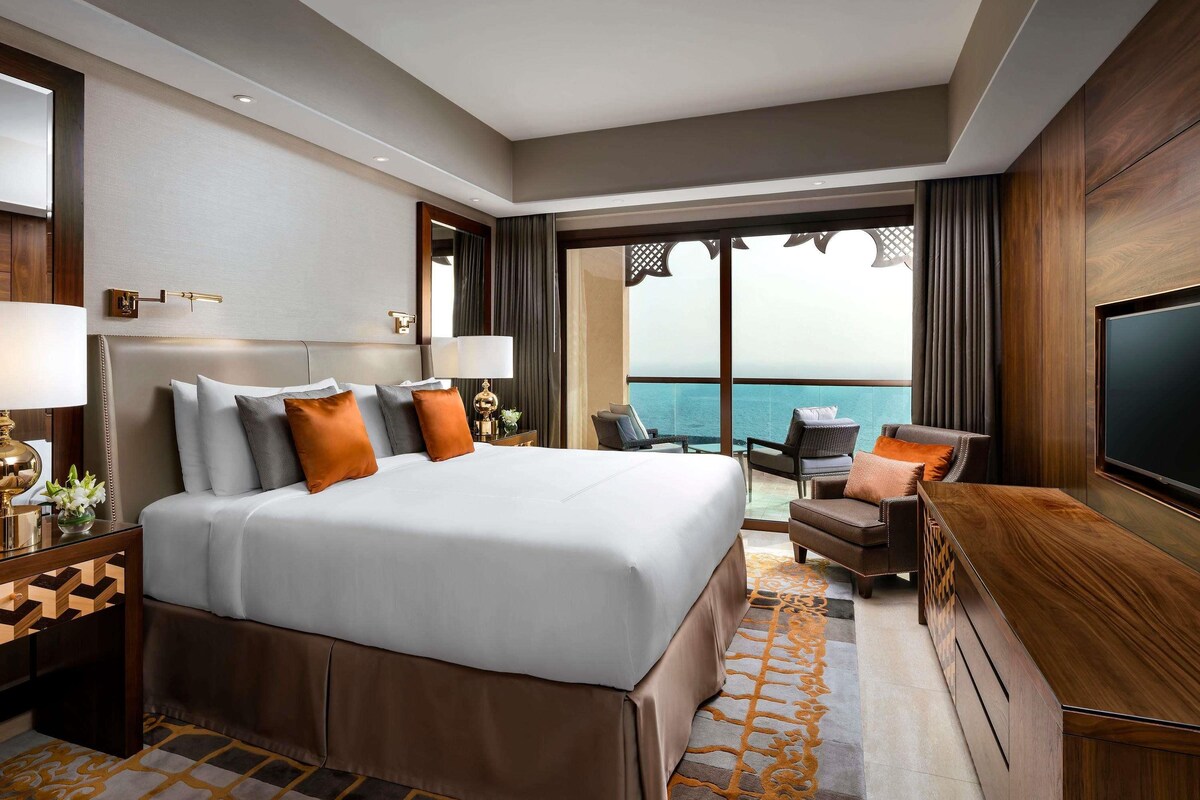 A hotel room with a large bed, a TV, a seating area with a view of the ocean, and a balcony.