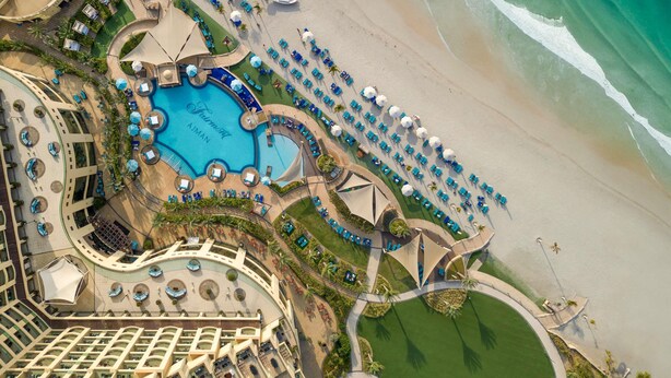 An aerial view of a resort with a central swimming pool, beachside lounge areas, and a beachfront. - Fairmont Ajman (Ajman)