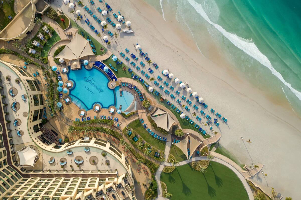 An aerial view of a resort with a central swimming pool, beachside lounge areas, and a beachfront.