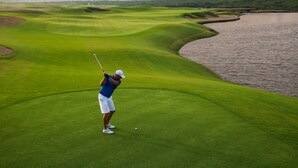 A golf course with a water hazard and a city skyline in the background. - Fairmont Ajman (Ajman)