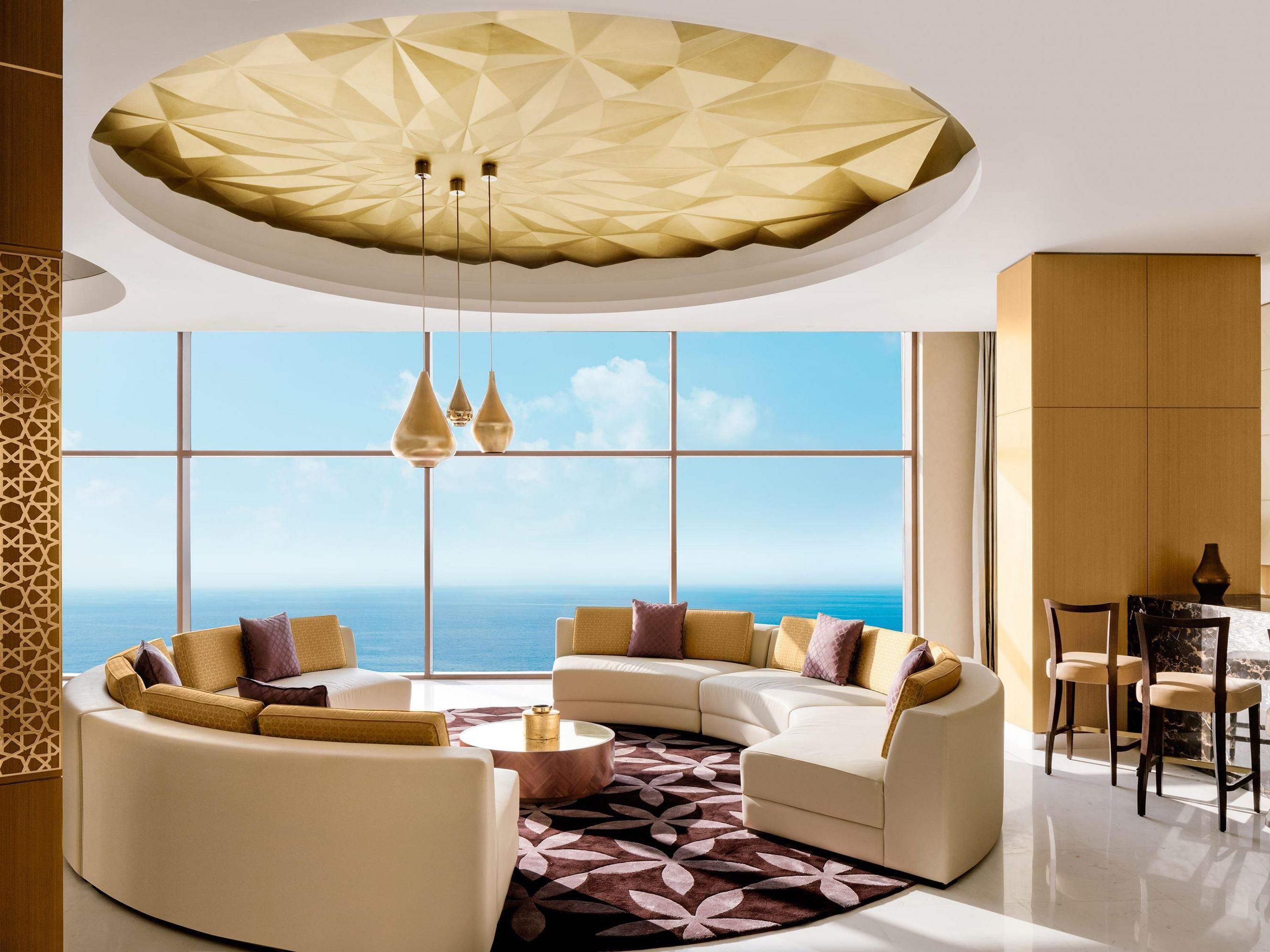 A modern living room with a curved sofa set, a round coffee table, and a view of the ocean through large windows.