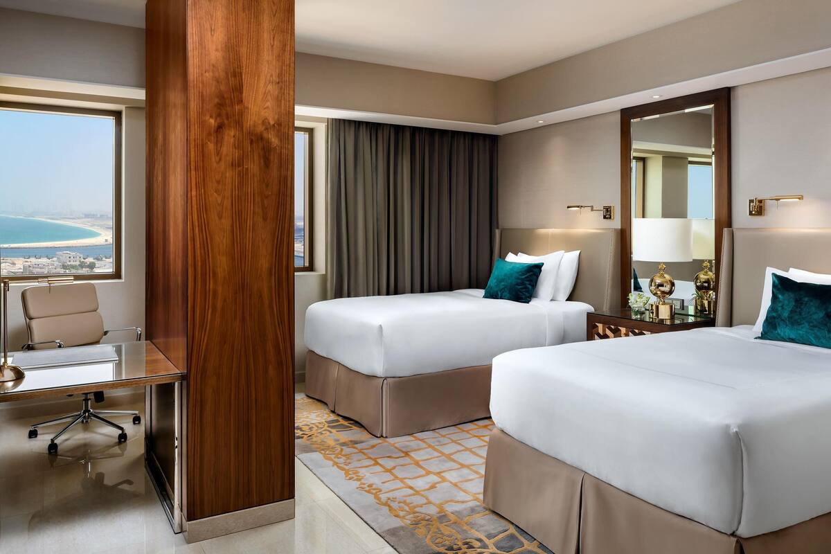 Une chambre d’hôtel avec deux lits, un bureau et une grande fenêtre donnant sur la mer.