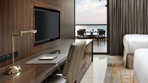 A hotel room with a large bed, a desk with a TV, a chair, and a view of the sea through a balcony. - Fairmont Ajman (Ajman)