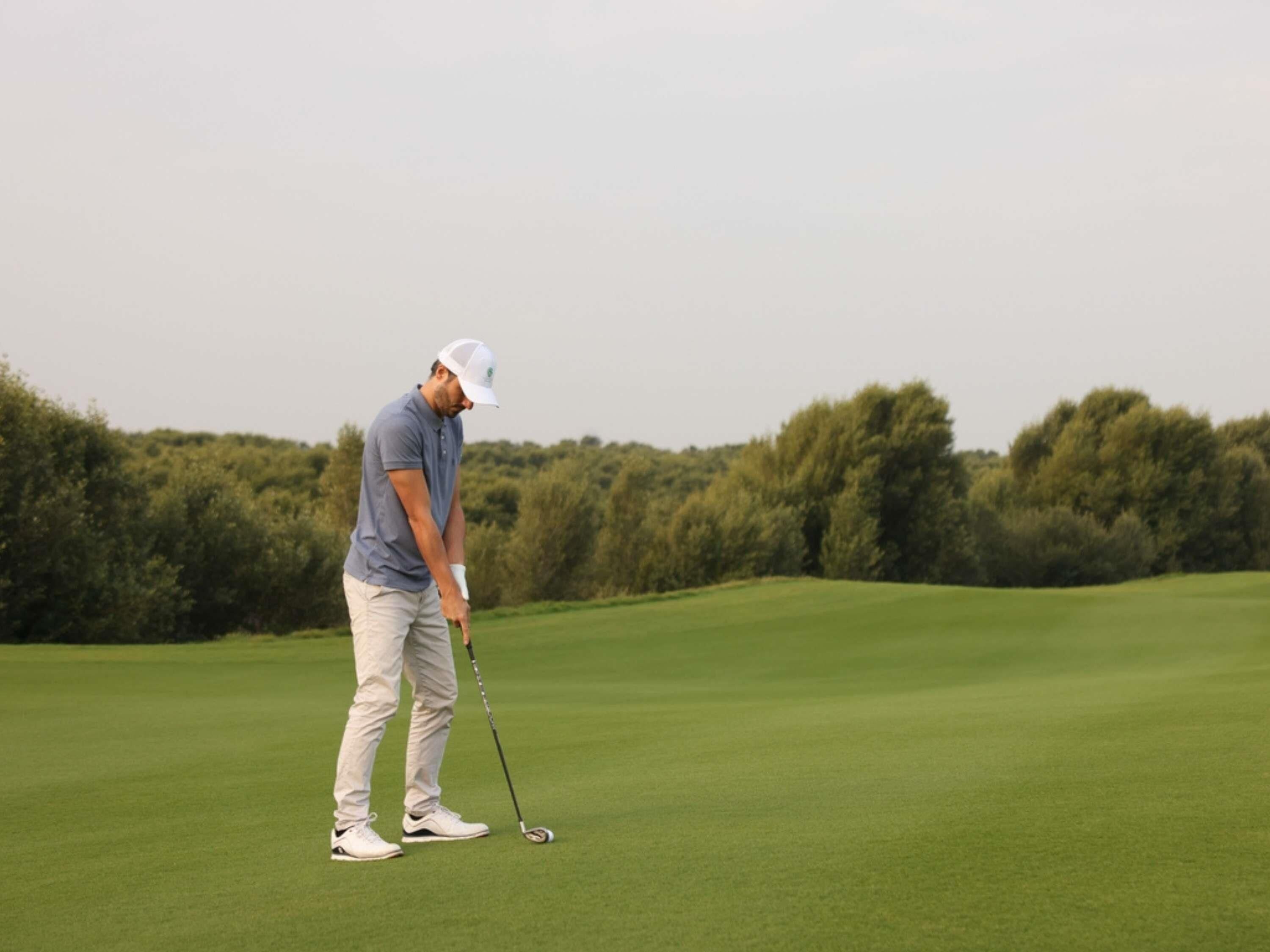 Eine Person auf einem Golfplatz, im Hintergrund Bäume.
