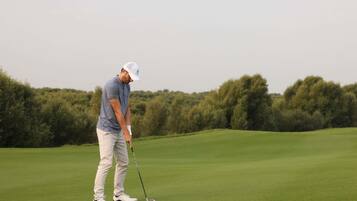 Eine Person auf einem Golfplatz, im Hintergrund Bäume.