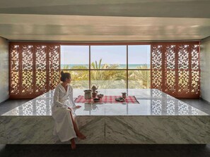 A woman sitting by a large window with a view of palm trees and the sea. - Fairmont Ajman (Ajman)