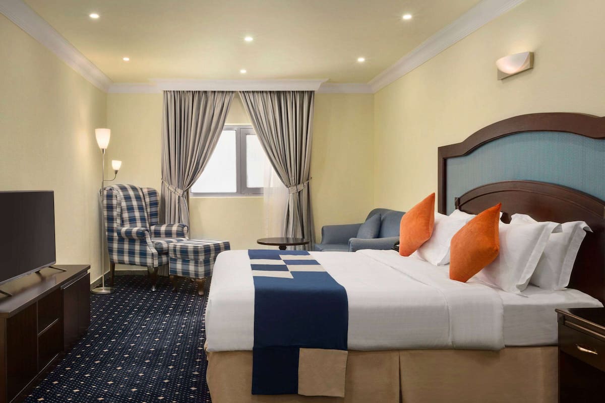 Une chambre d’hôtel avec un lit, une chaise, une télévision et une fenêtre avec des rideaux.