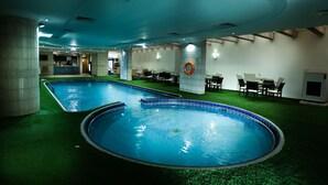 Una piscina interior con dos zonas separadas, rodeada de áreas de descanso y una recepción.