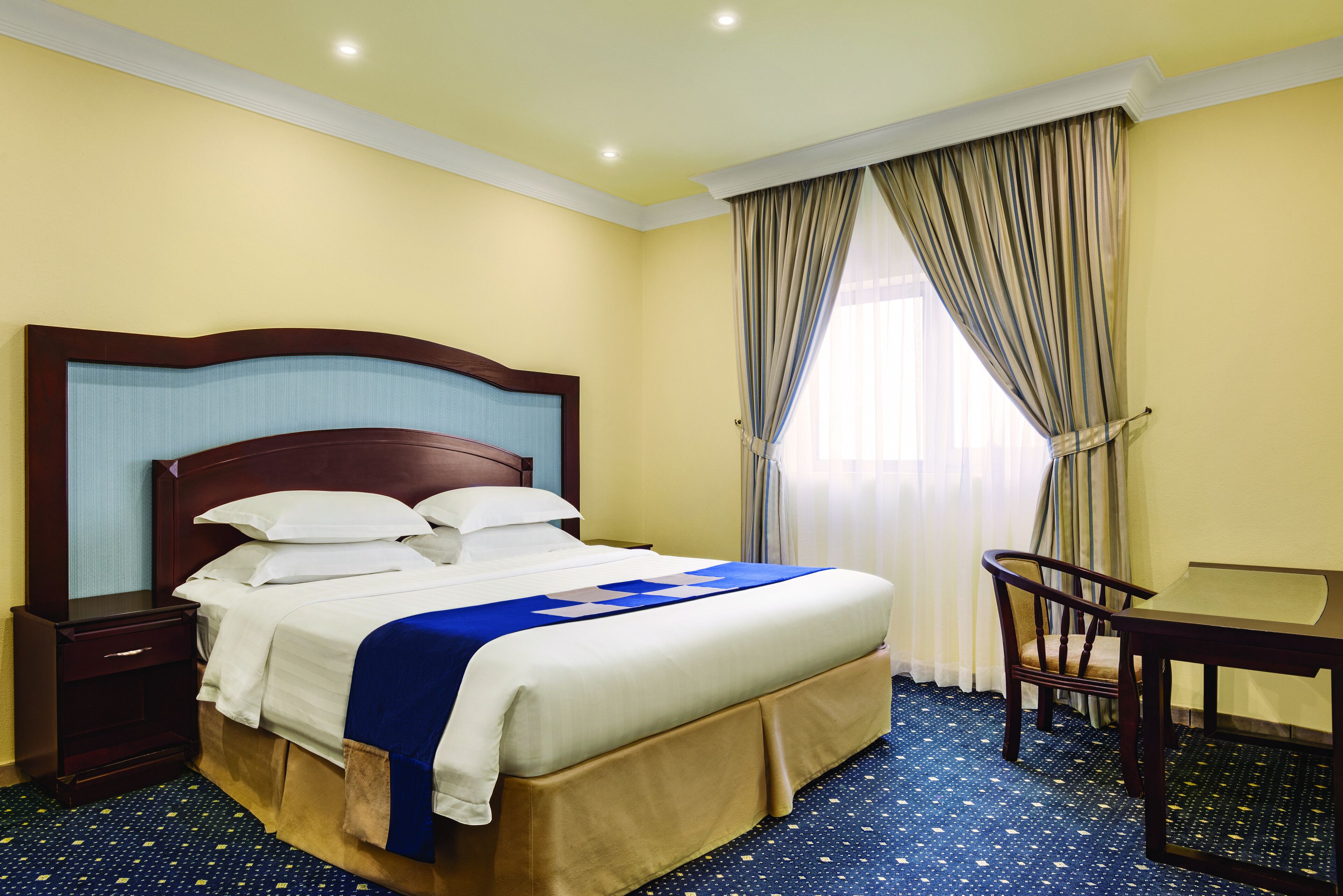 Habitació d'hotel amb un llit gran, una nitzeta de fusta, una cadira i una taula petita.