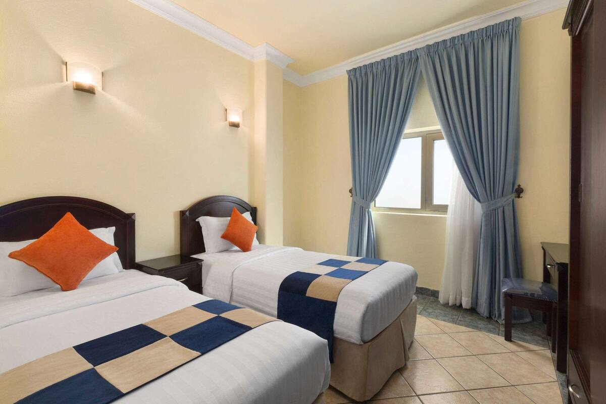 Une chambre d’hôtel avec deux lits, une table de chevet, une chaise et une fenêtre avec des rideaux.