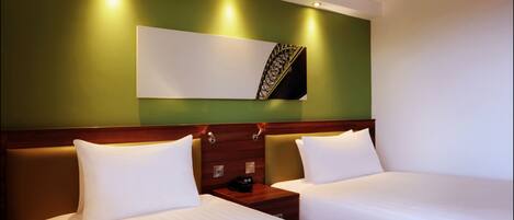 A hotel room with two beds, a wooden headboard, a nightstand, and a wall-mounted artwork.