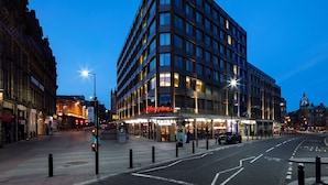 Ein modernes Hotel mit Eckgebäude, großen Fenstern und einem gut beleuchteten Eingang.