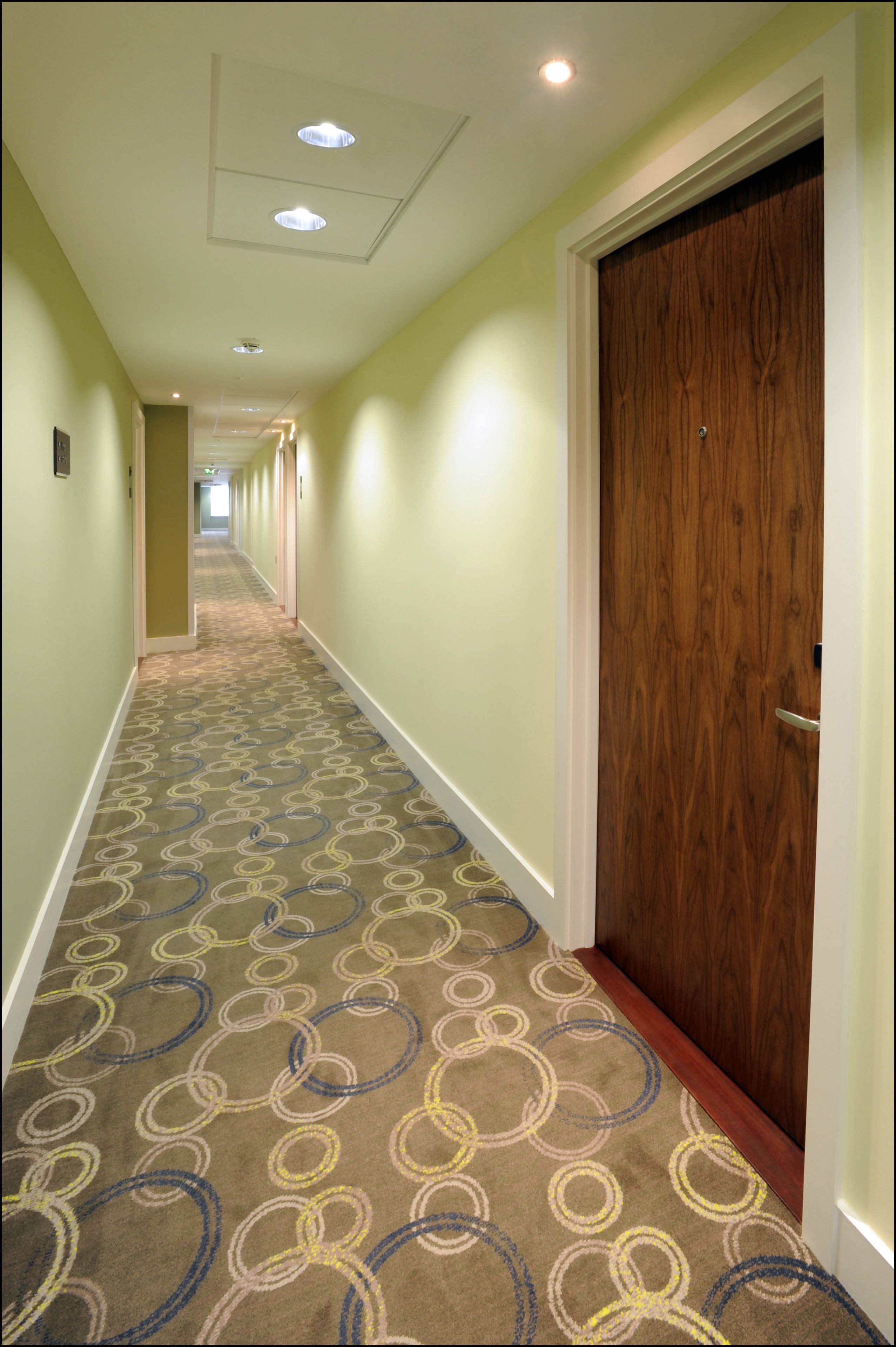 A hallway with patterned carpet, wooden doors, and recessed lighting.
