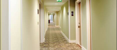 A hotel hallway with patterned carpet, green walls, and doors on both sides.