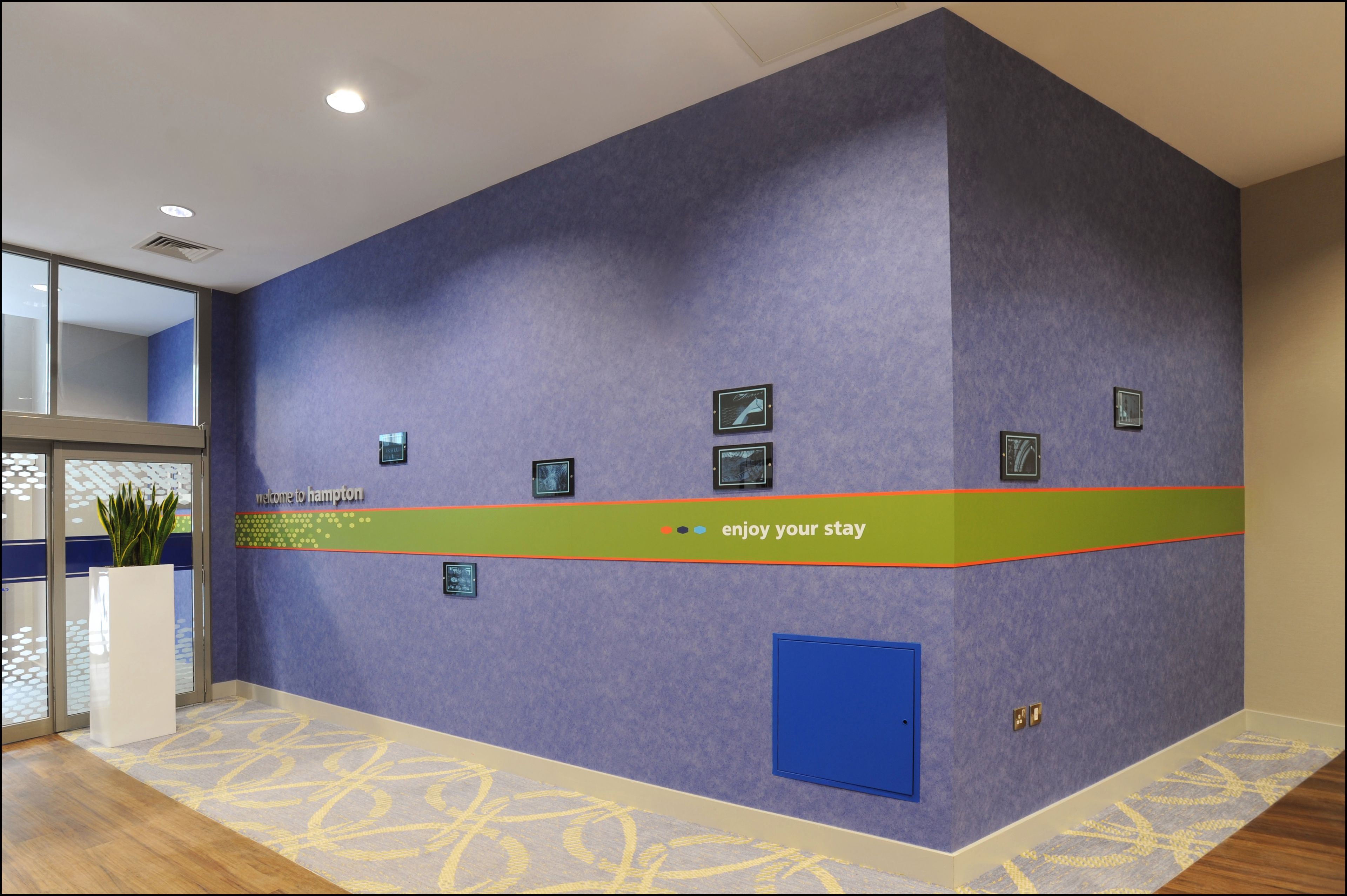 Ein Empfangsbereich mit blauer Wand, einem Willkommensschild und einem grünen Streifen mit dem Schriftzug "enjoy your stay".