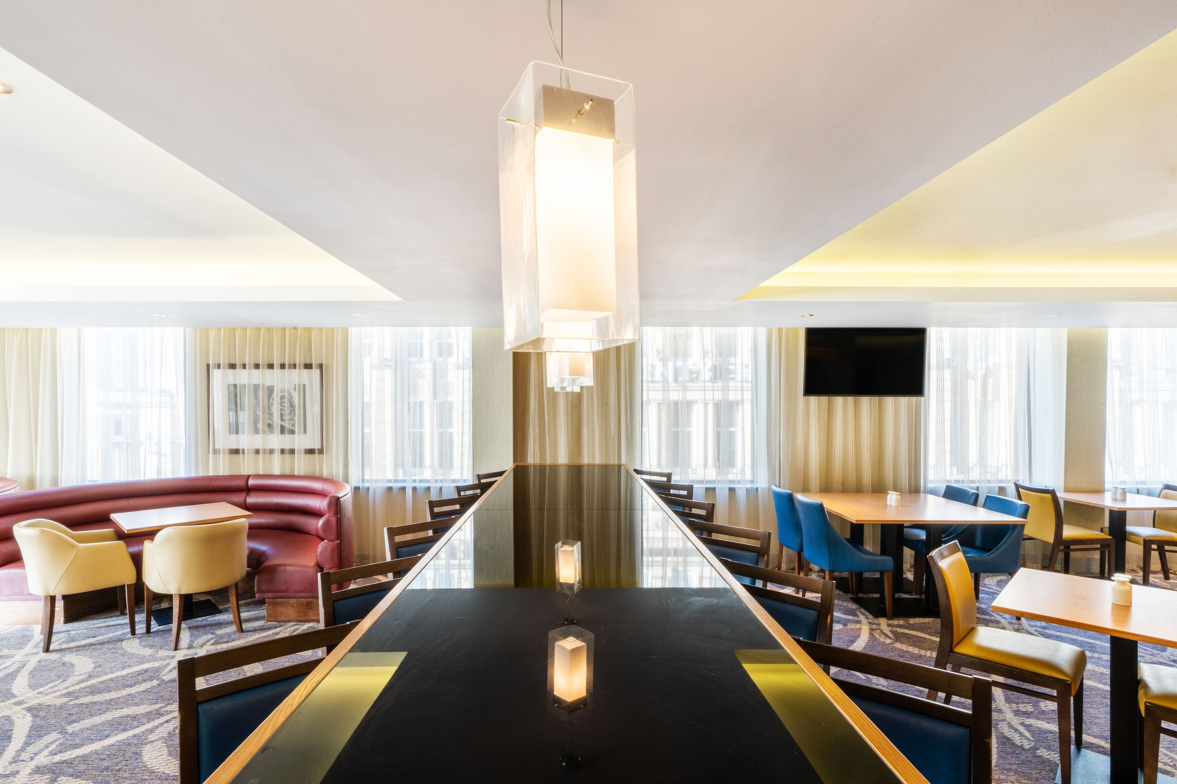 Un comedor moderno de hotel con una mesa larga, asientos cómodos y ventanas amplias.
