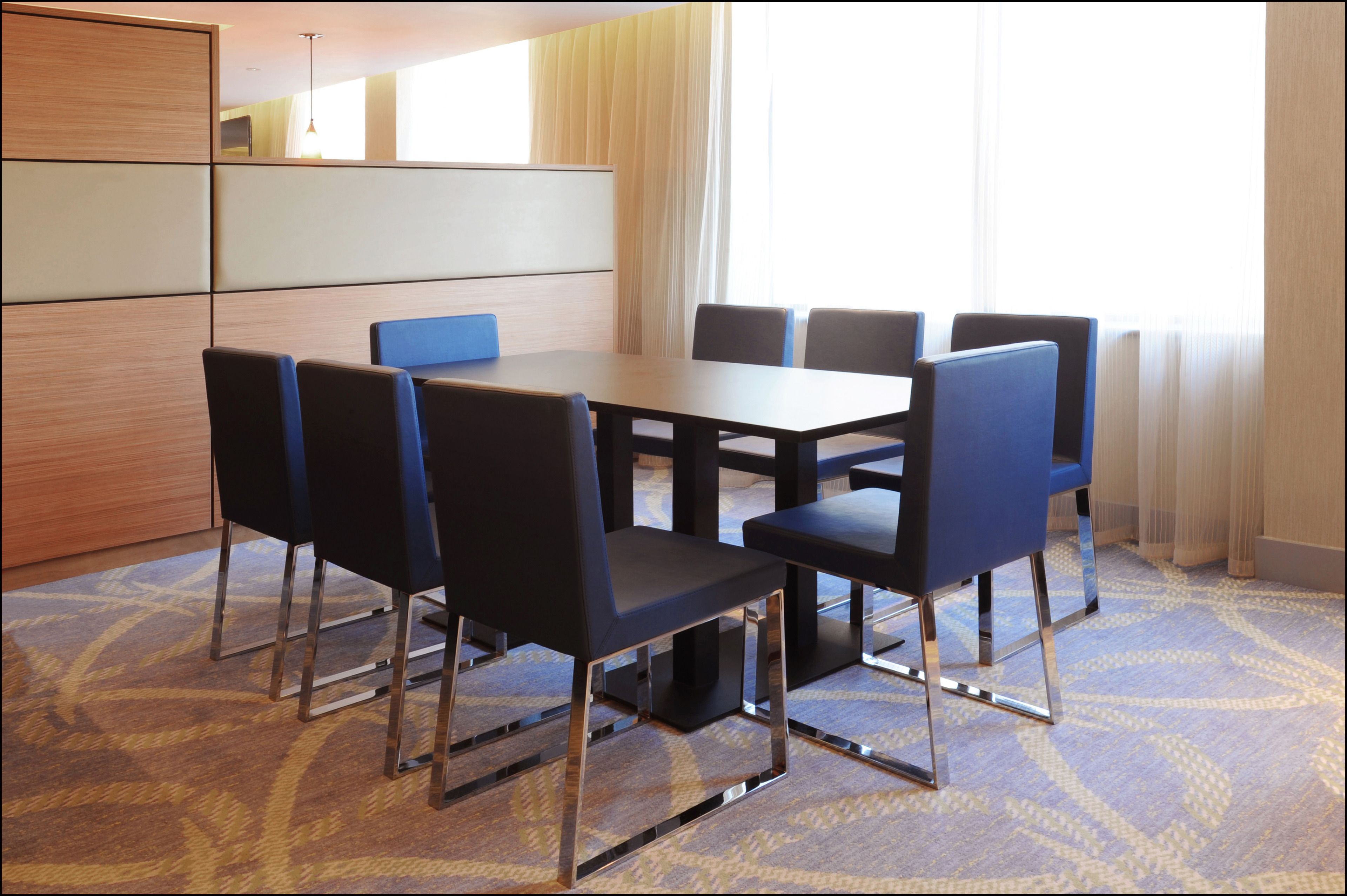 A conference room with a rectangular table and six chairs, a wooden cabinet, and a large window with sheer curtains.