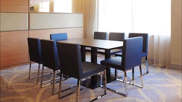 A conference room with a rectangular table and six chairs, a wooden cabinet, and a large window with sheer curtains.