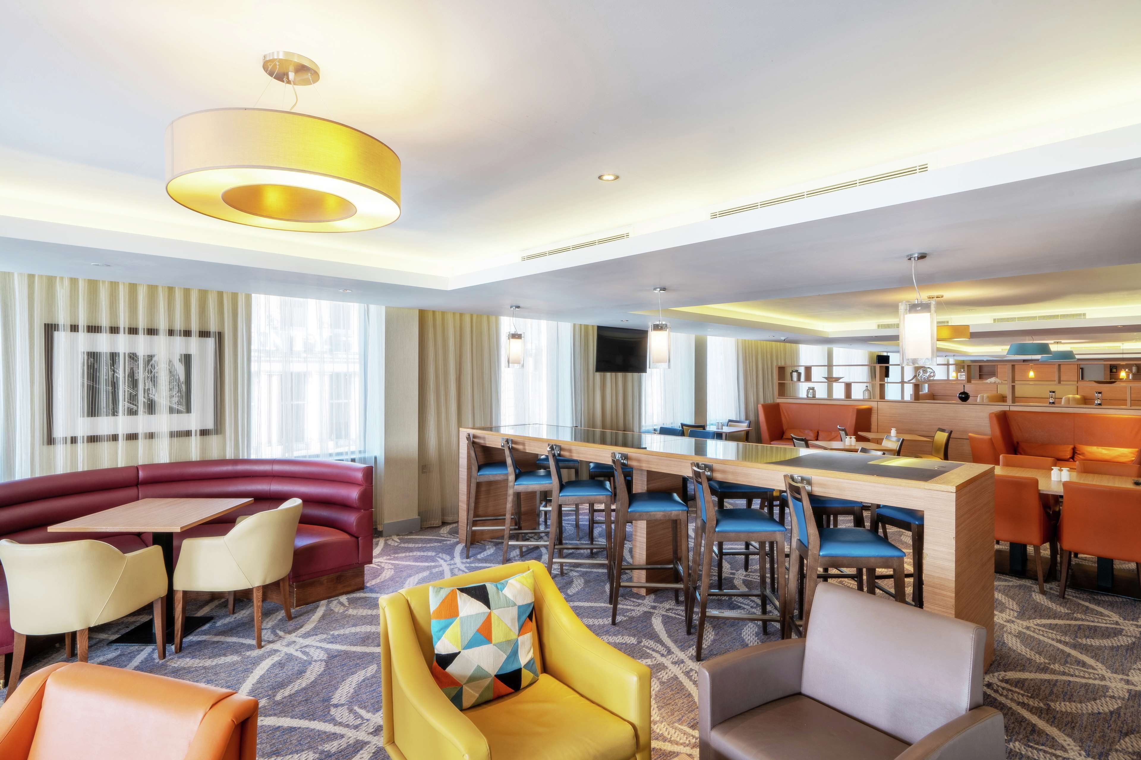 Een hotel lobby met een bar, zitgedeelte en een televisiescherm.