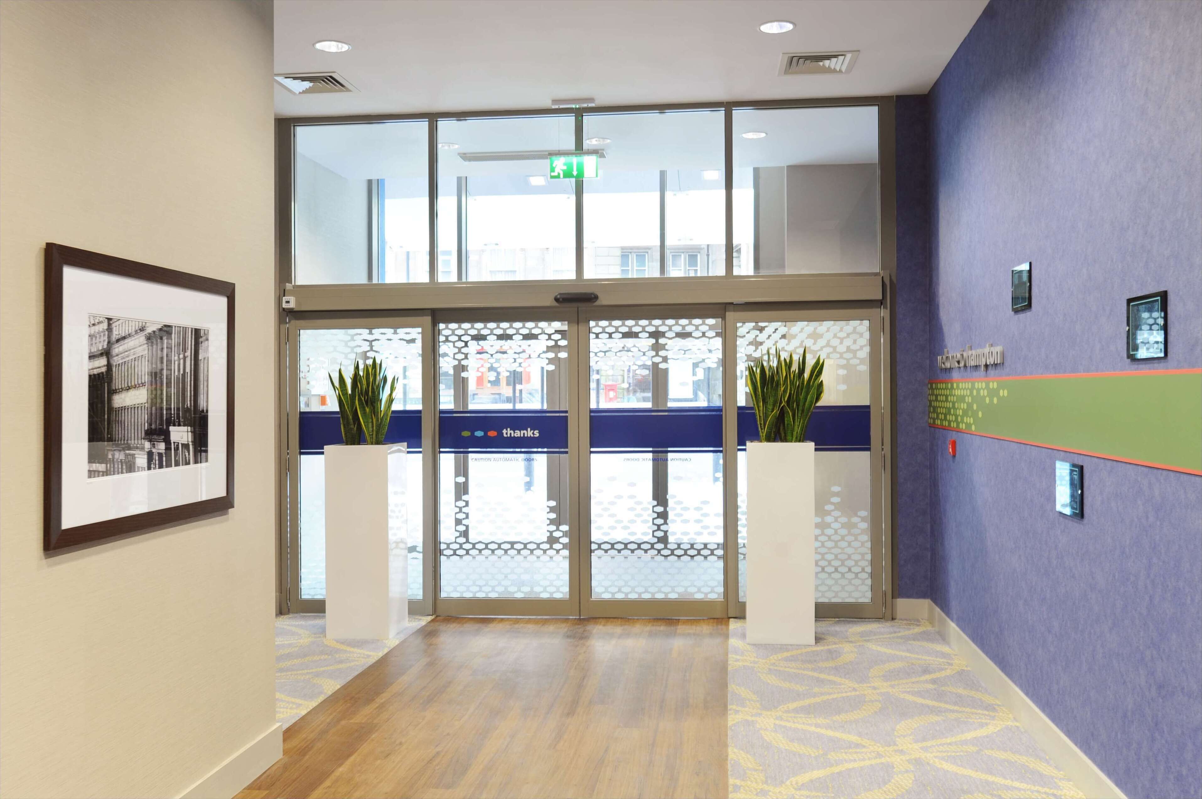 L’entrée d’un hôtel, avec une porte en verre, des œuvres d’art encadrées, des plantes en pot et un comptoir d’accueil.