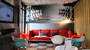 Un espacio de descanso moderno con un sofá rojo, sillas color esmeralda y una alfombra estampada.
