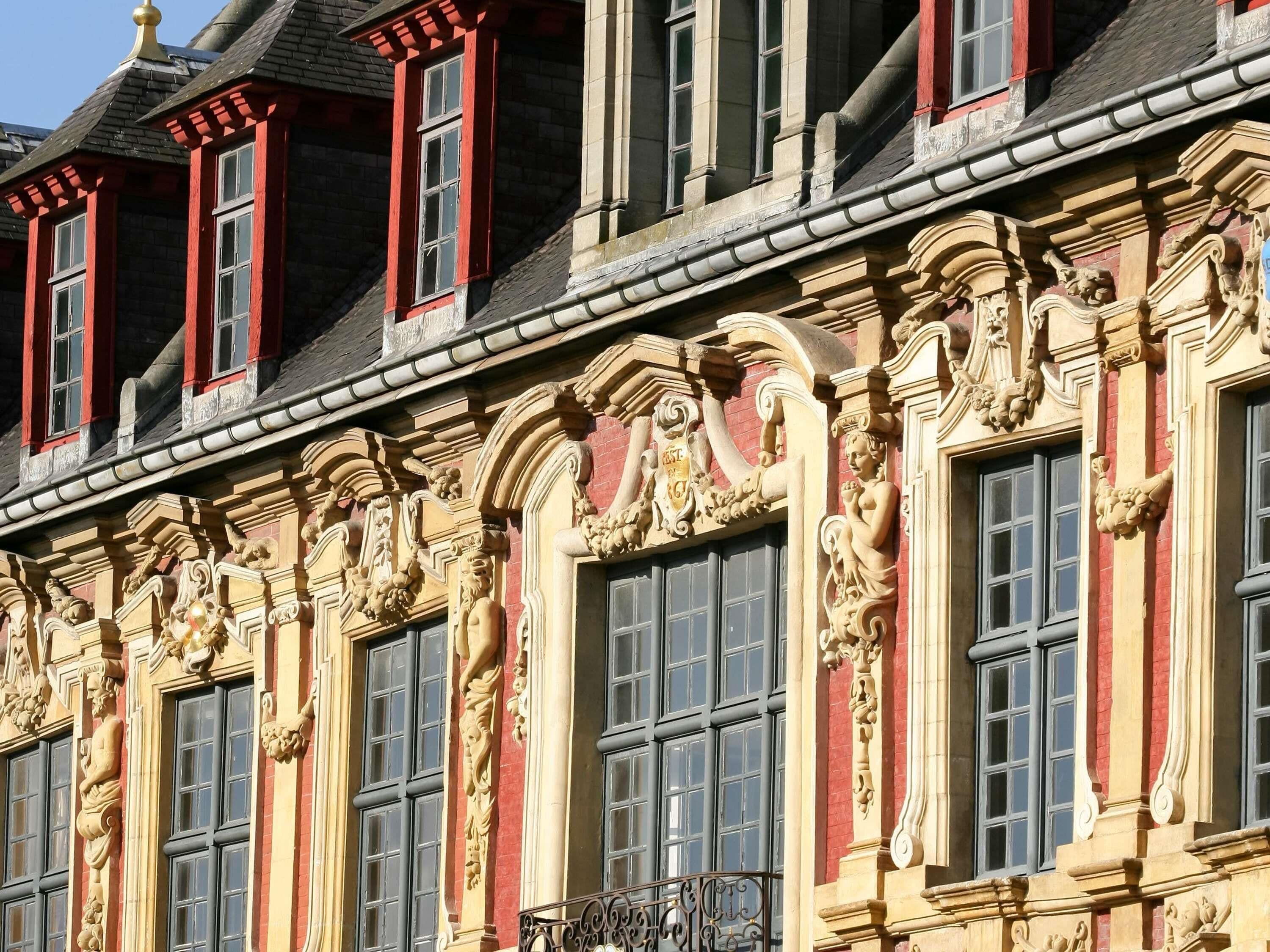 A building with ornate architectural details, including sculptural decorations around windows and a balcony with wrought iron railings.