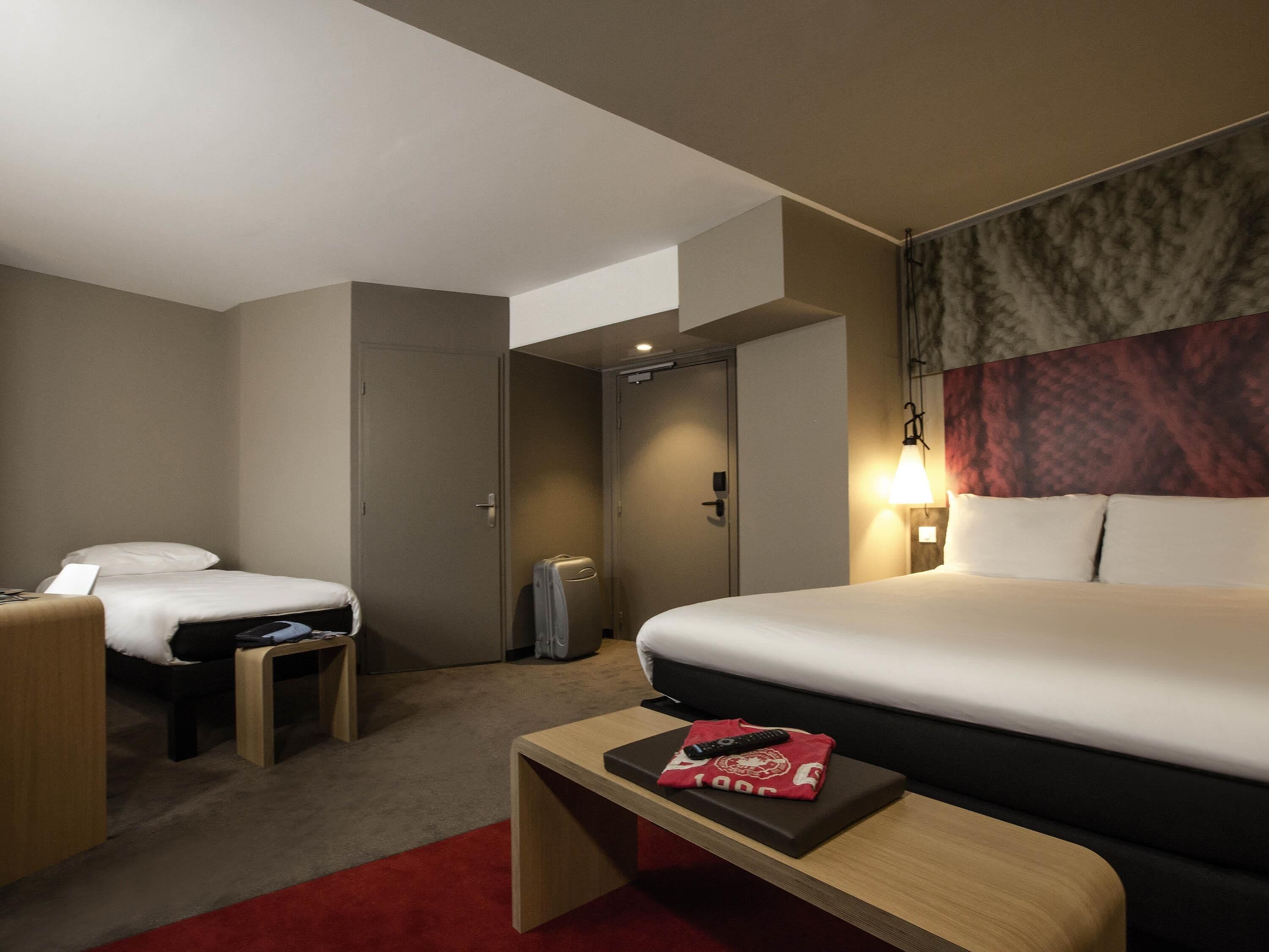 A hotel room with a large bed, two smaller beds, a desk, and a red carpet.