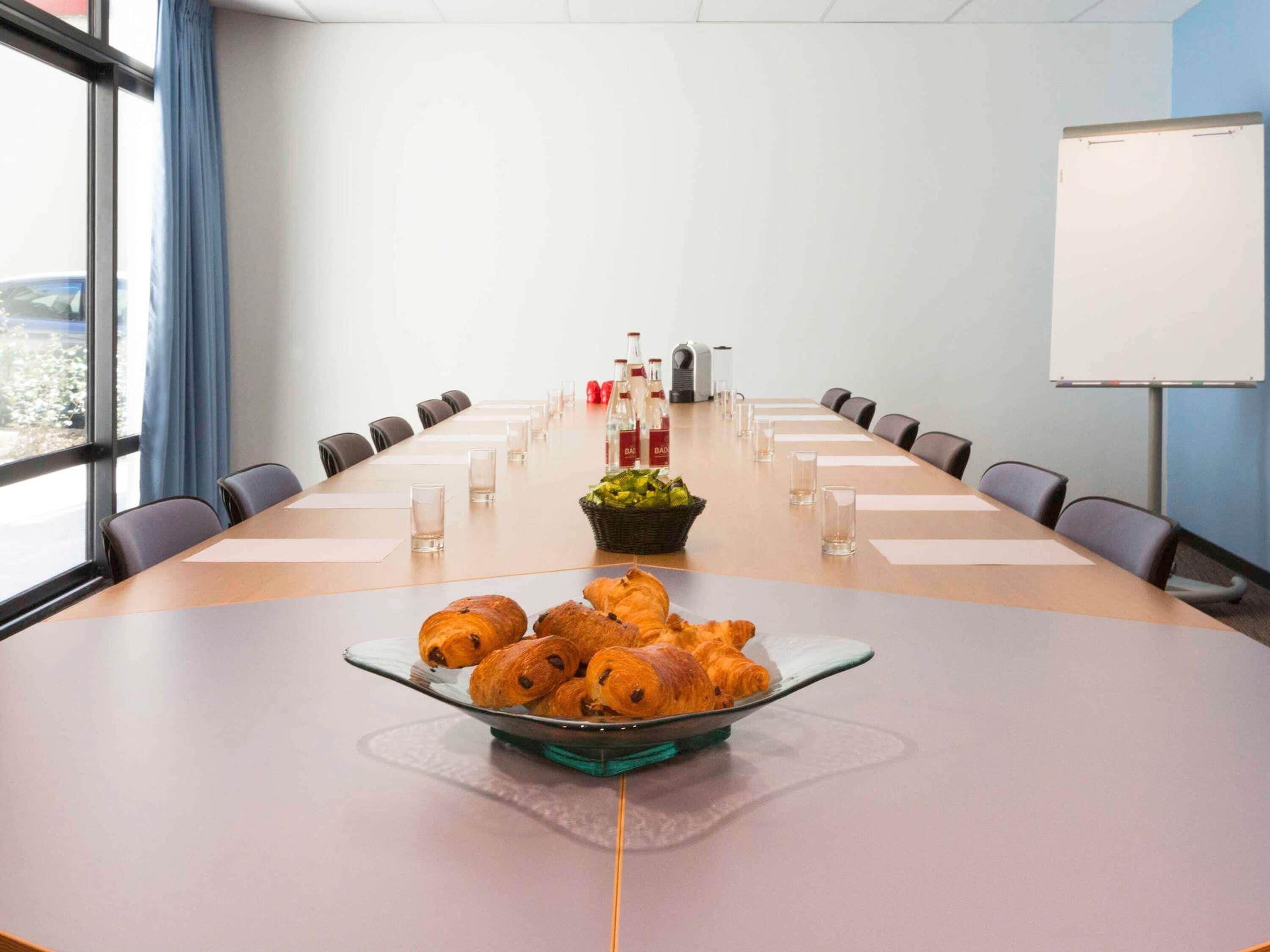 A conference room with a long table, chairs, a whiteboard, and a bowl of croissants.