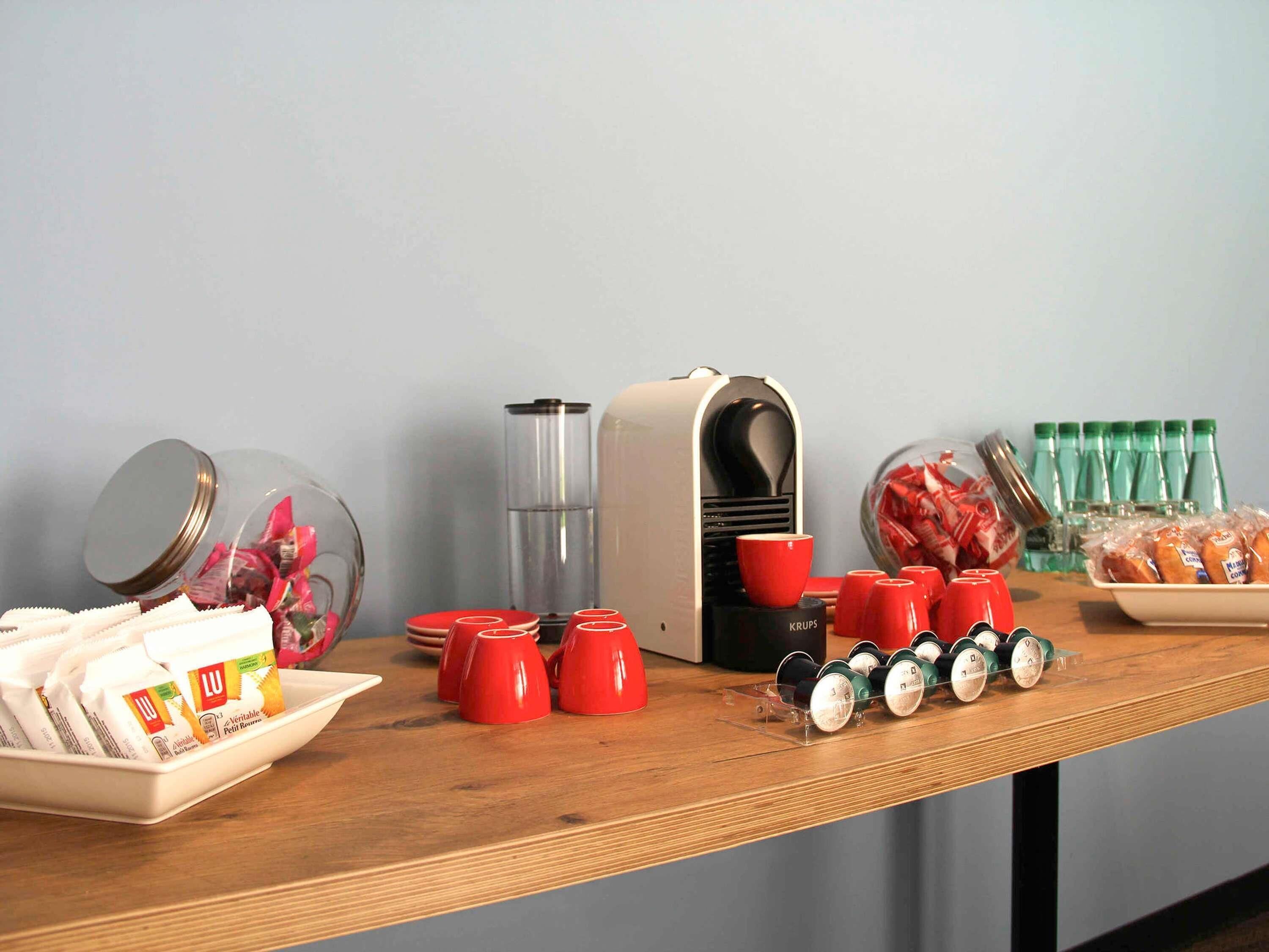 A buffet setup with food items, red cups, a coffee machine, and a water dispenser on a wooden table.