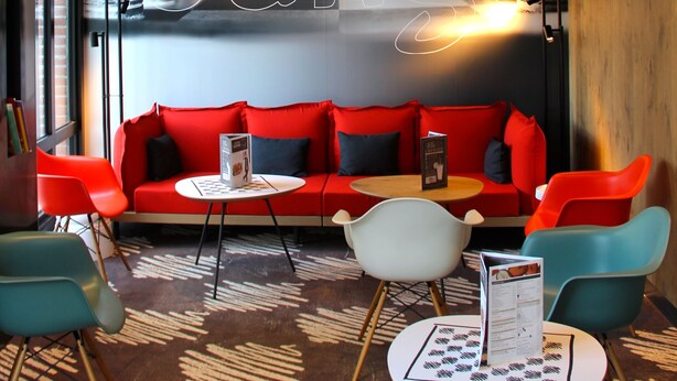 Un área de descanso moderna con un sofá rojo, sillas color turquesa y una alfombra estampada.
