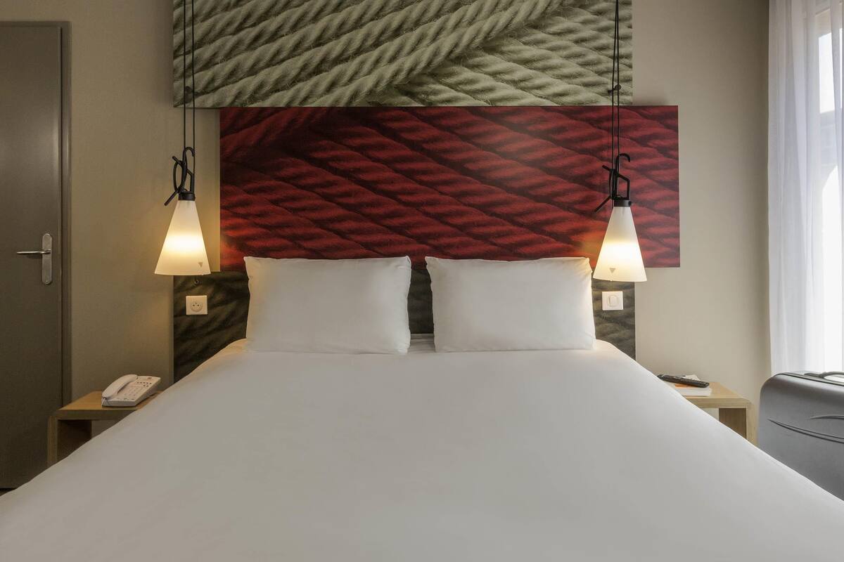 A hotel room with a bed, two bedside lamps, a telephone, and a suitcase.
