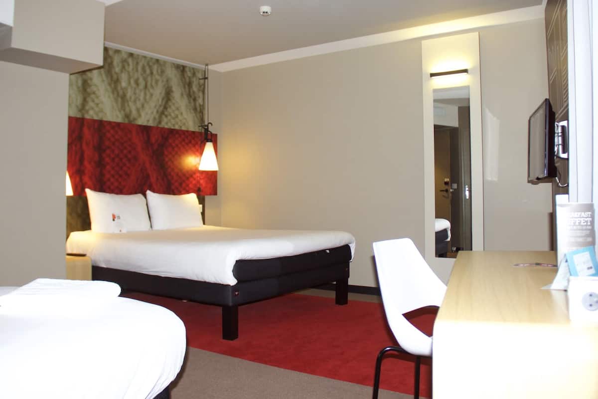 Ein Hotelzimmer mit Bett, Schreibtisch, Stuhl, Fernseher und einem roten Teppich.