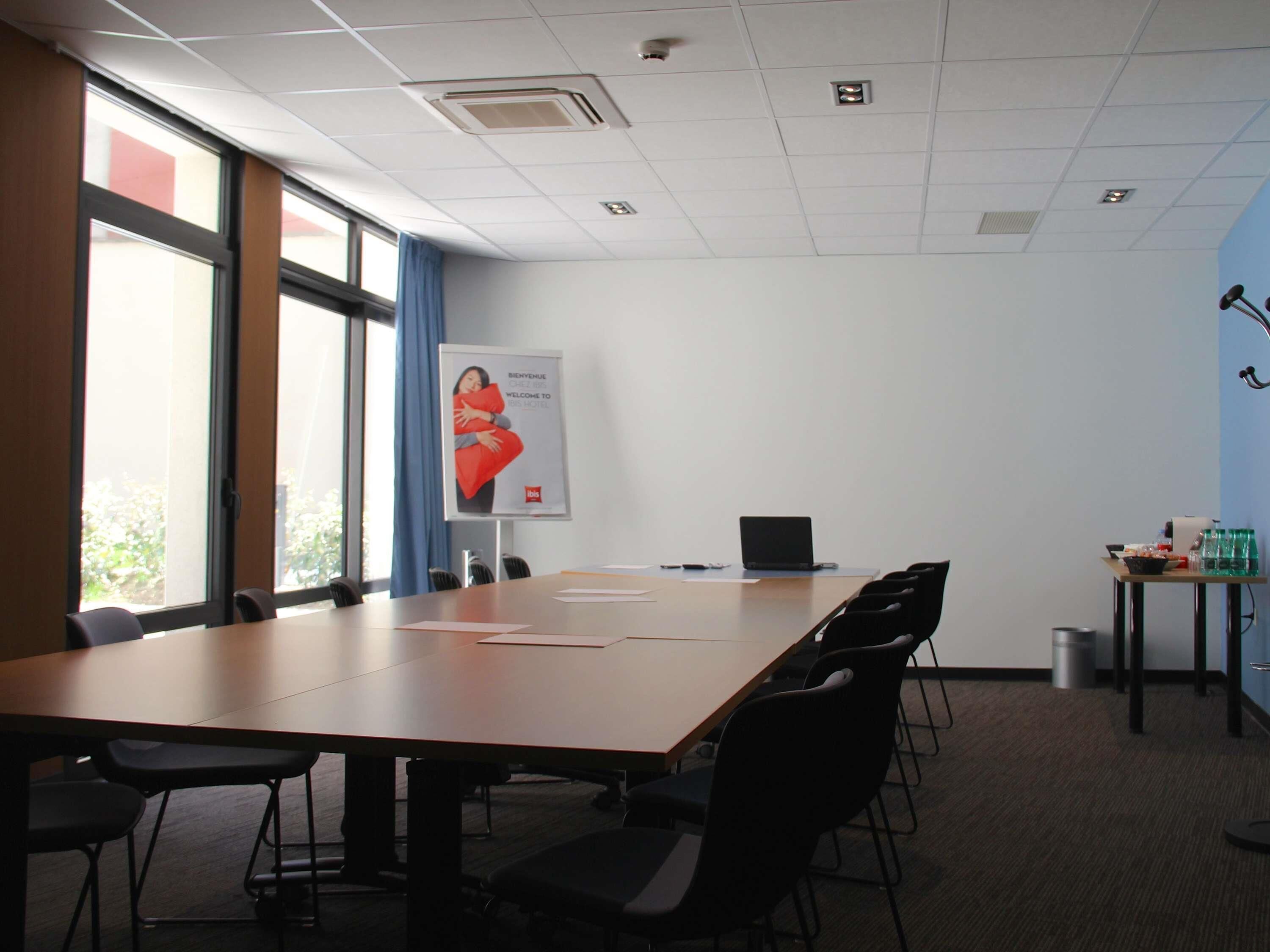 Un salón de conferencias con una larga mesa, sillas, una computadora portátil y un cartel en la pared.