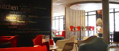 A modern restaurant interior with round tables and colorful chairs, a blackboard with nutritional information, and large windows allowing natural light.