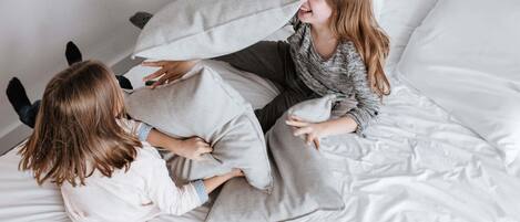 A bed with white bedding and pillows, a person sitting on the bed, and another person lying down.