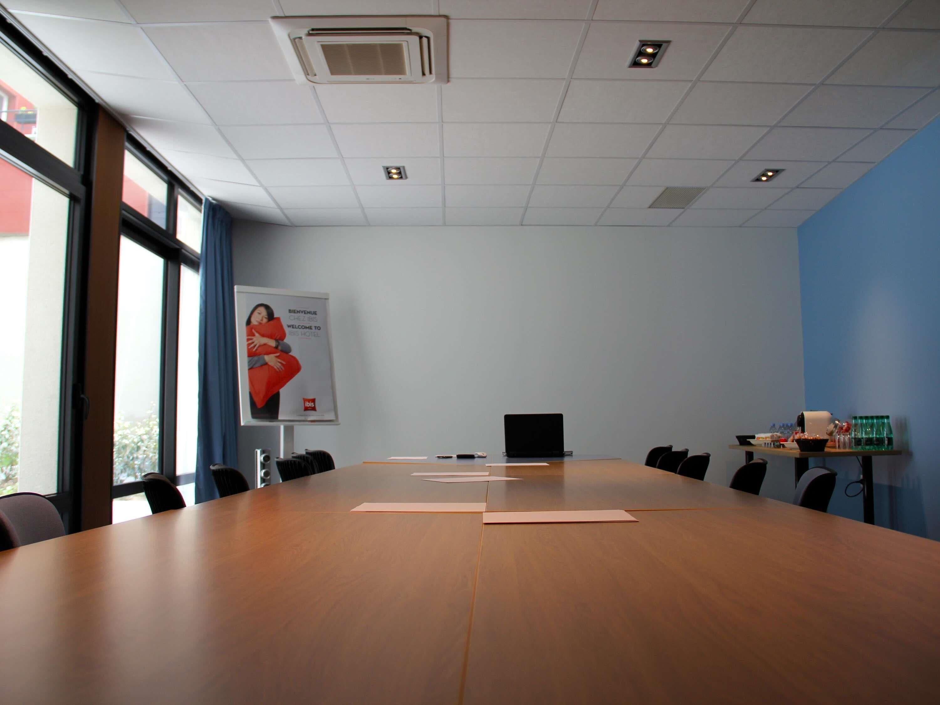 A conference room with a long table, chairs, a laptop, a poster, and a water dispenser.