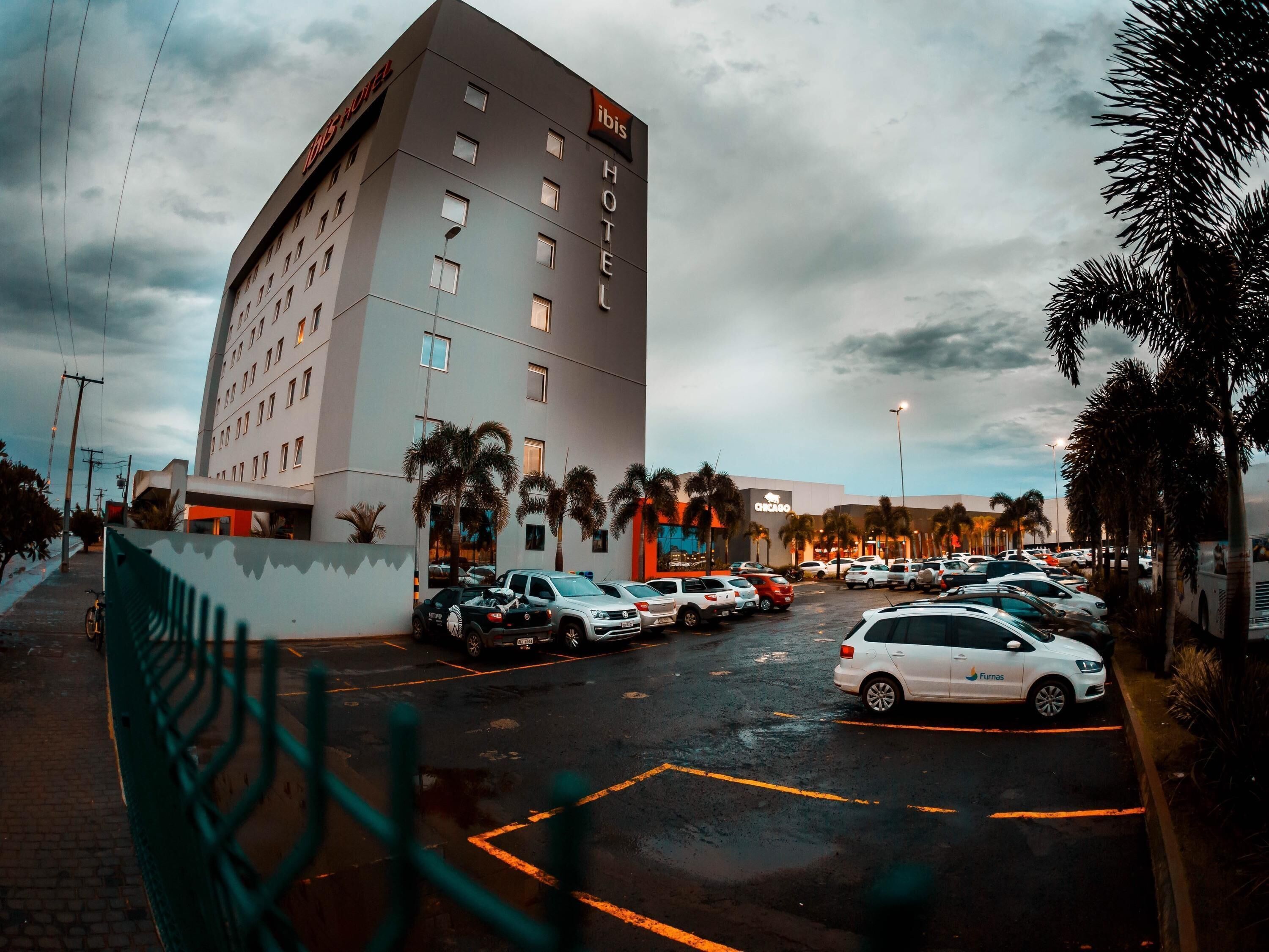 Un hôtel à plusieurs étages, un parking avec plusieurs voitures et des palmiers.
