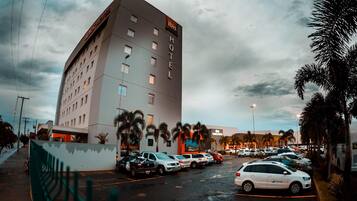 Un hôtel à plusieurs étages, un parking avec plusieurs voitures et des palmiers.